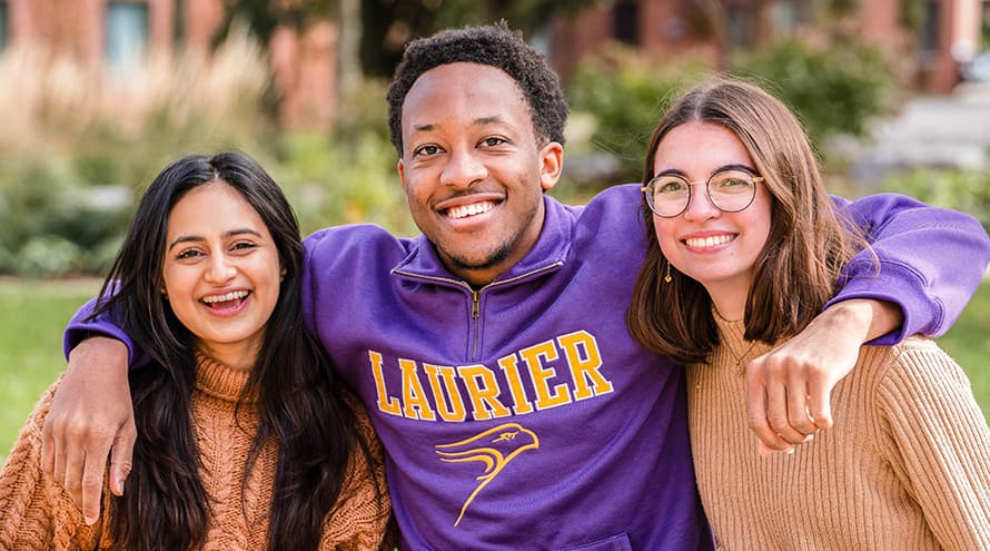 Three Laurier students with their arms around each other smiling at the camera